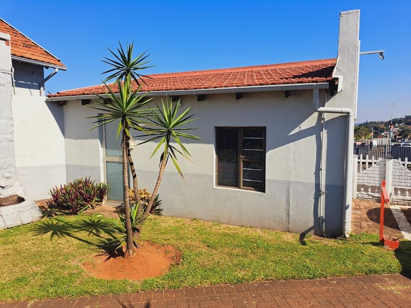 Rear exterior view of the property featuring a tiled roof, external chimney, and paved garden area.