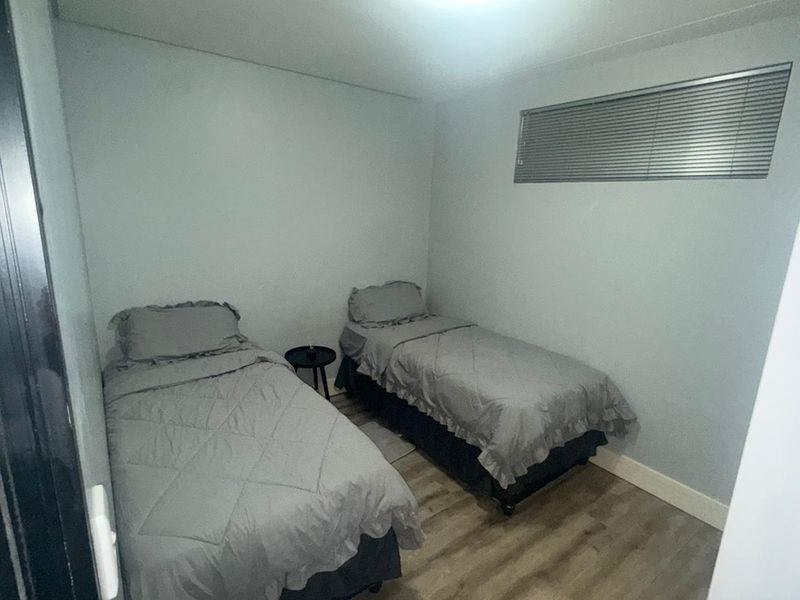 A compact bedroom featuring light-toned laminate flooring and a high-set window with fitted horizontal blinds.