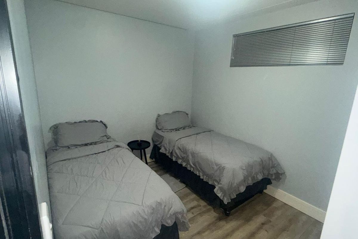 A compact bedroom featuring light-toned laminate flooring and a high-set window with fitted horizontal blinds.