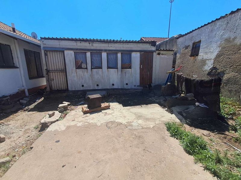 Rear exterior view of the property featuring a concrete patio area and a detached structure requiring maintenance and exterior refurbishment.