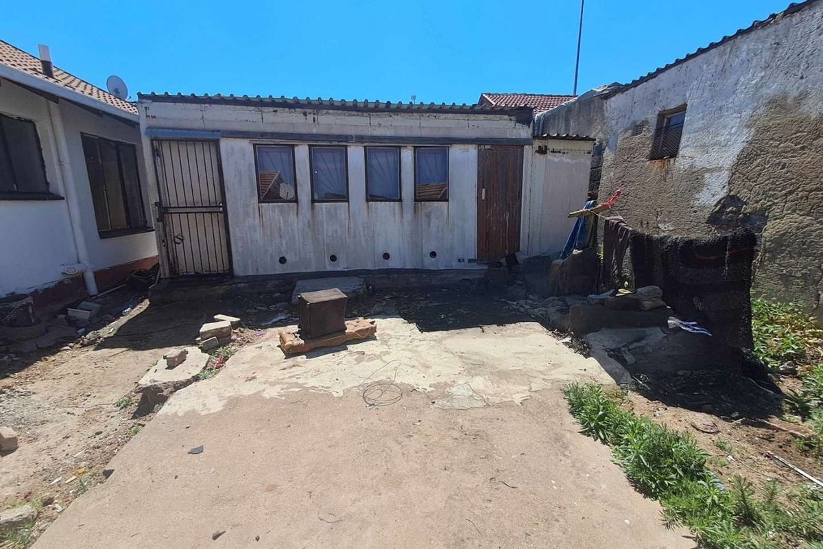 Rear exterior view of the property featuring a concrete patio area and a detached structure requiring maintenance and exterior refurbishment.