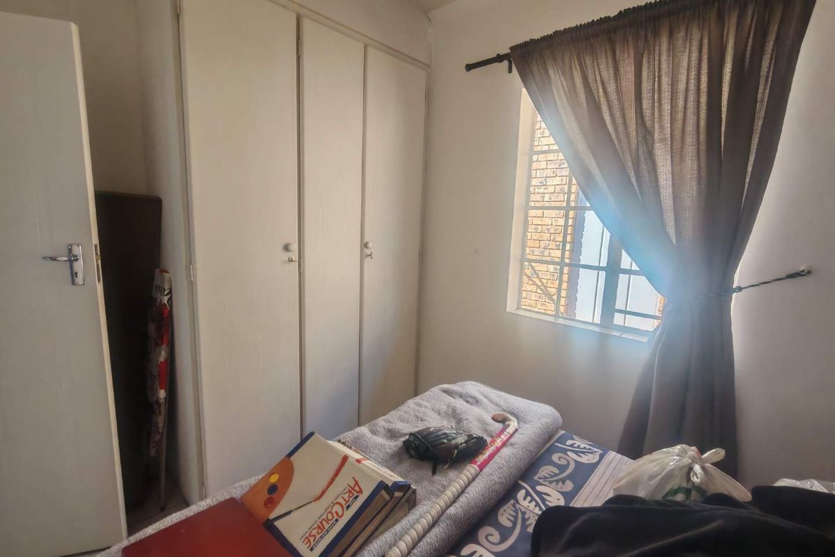 A functional bedroom featuring built-in cupboards and a window with security bars, offering a practical layout for a townhouse setting.