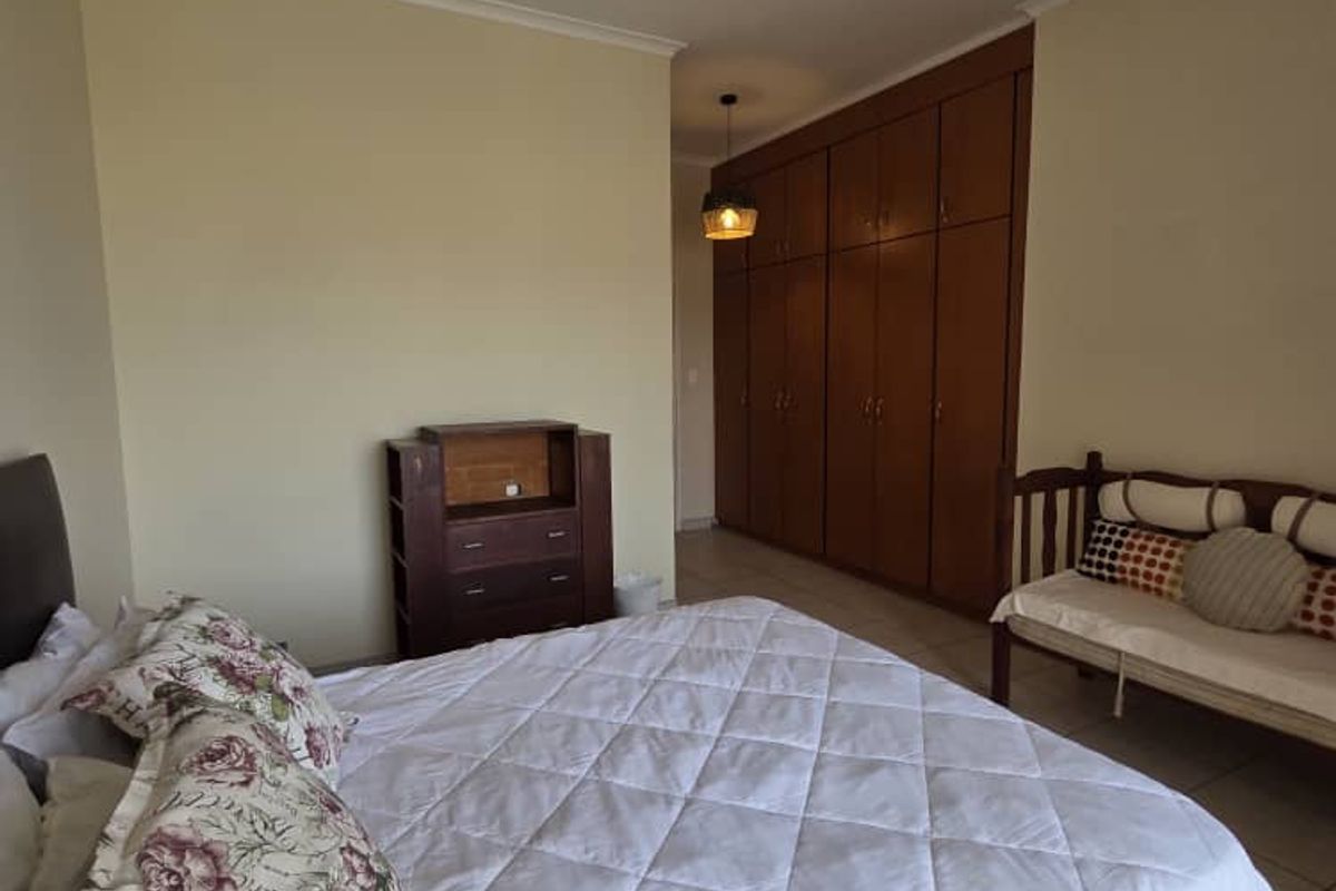 A spacious bedroom featuring built-in wooden cupboards, tiled flooring, and a ceiling fan light fixture.