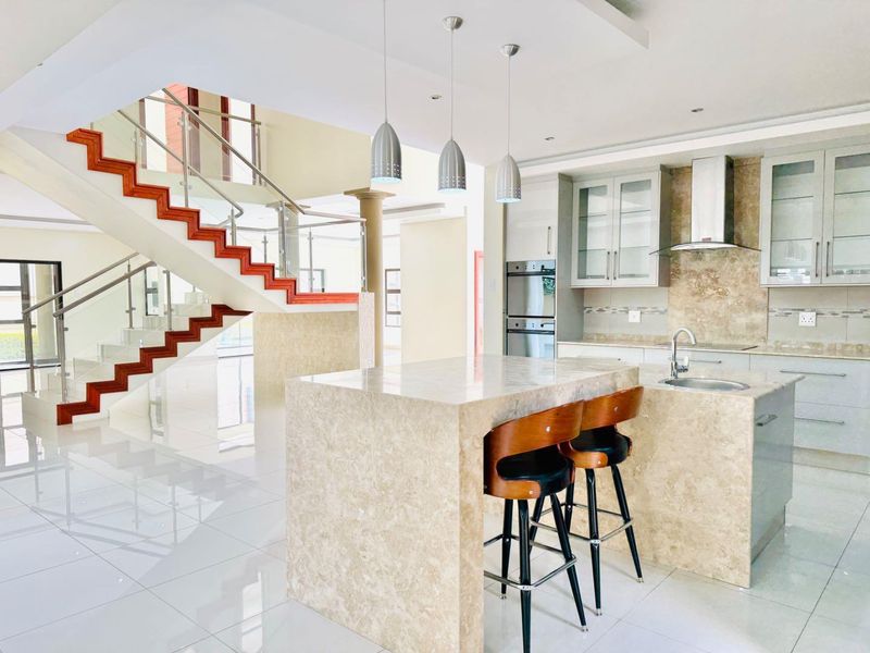 Modern open-plan kitchen featuring a stone island, built-in appliances, and sleek cabinetry, seamlessly integrated with a striking wooden staircase and glass balustrade.