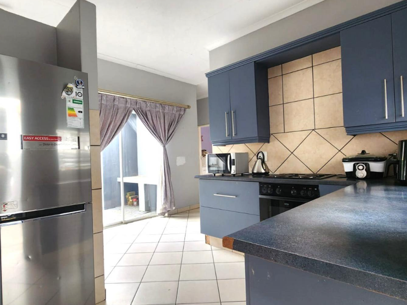 A functional kitchen featuring blue cabinetry, dark laminate countertops, a built-in oven with gas hob, and tiled flooring with direct access to an outdoor area.