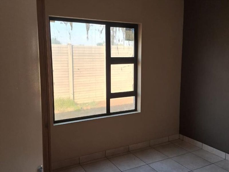 An empty bedroom featuring neutral wall tones, tiled flooring, and an aluminium window frame, offering a blank canvas for personalization.
