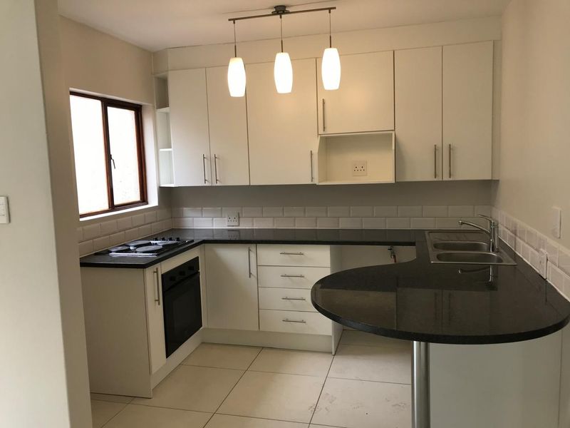 Modern kitchen featuring white cabinetry, dark granite countertops, a breakfast bar, built-in oven, hob, and subway tile backsplash.