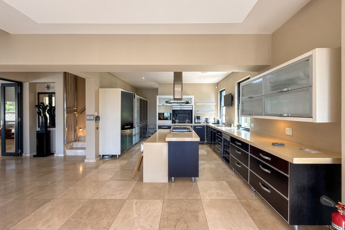 Modern kitchen featuring a central island, stone countertops, dark cabinetry, built-in appliances, and large format floor tiles in an open-plan layout.