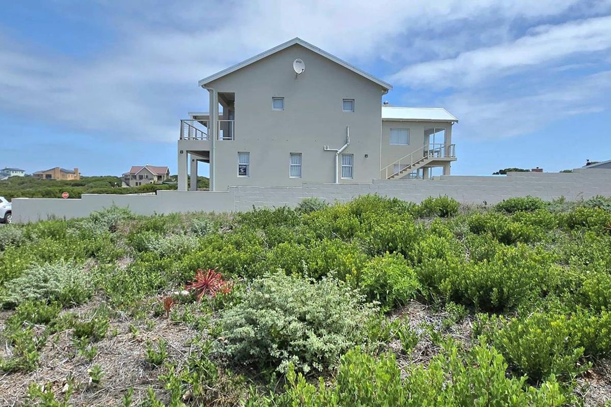 View of the residential property exterior from the adjacent vacant land, featuring a multi-level structure with balconies and a perimeter boundary wall.