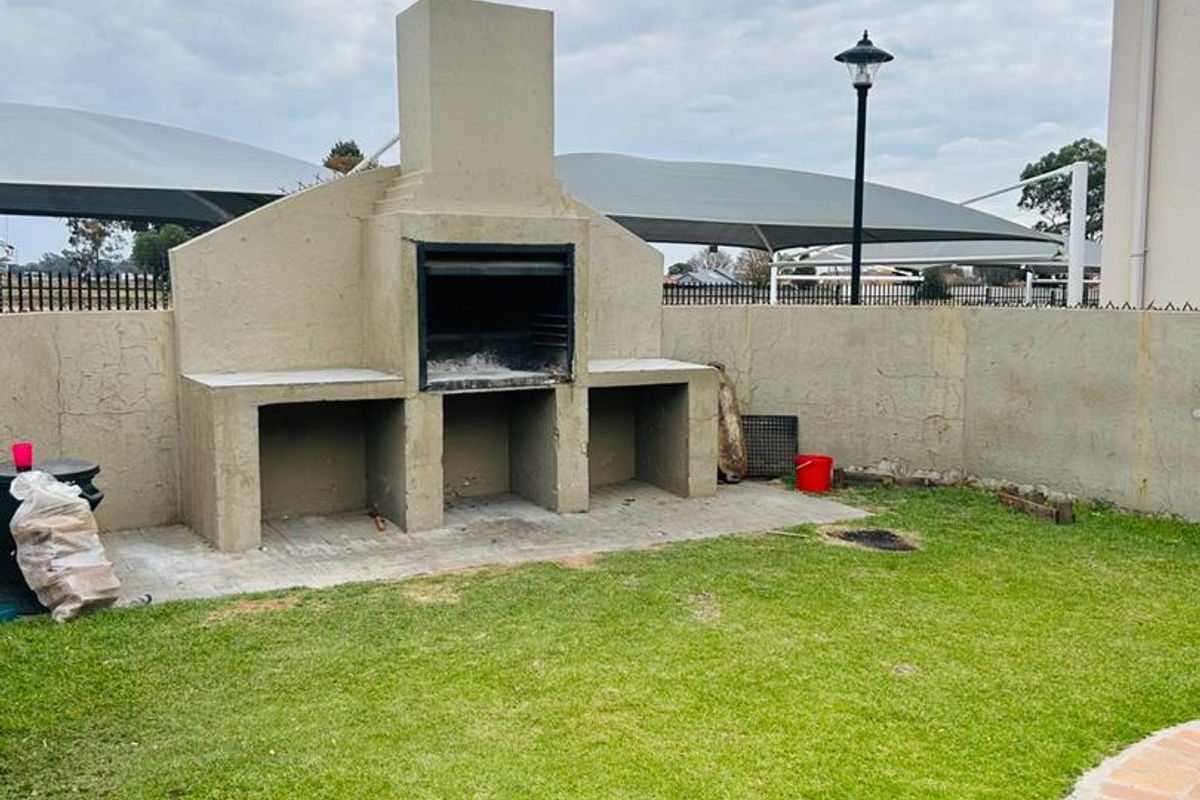 A private rear garden featuring a built-in masonry braai area with a chimney, set against a boundary wall with a small lawn and paved section.