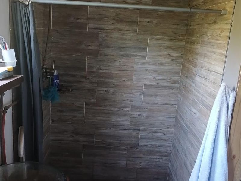 A rustic bathroom shower area featuring wood-look wall tiles, a modern vessel sink, and an exposed ceiling structure.