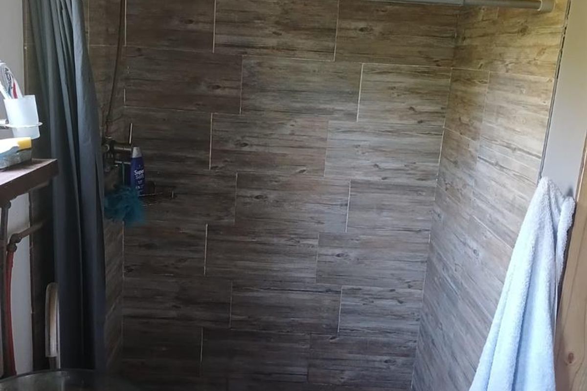 A rustic bathroom shower area featuring wood-look wall tiles, a modern vessel sink, and an exposed ceiling structure.