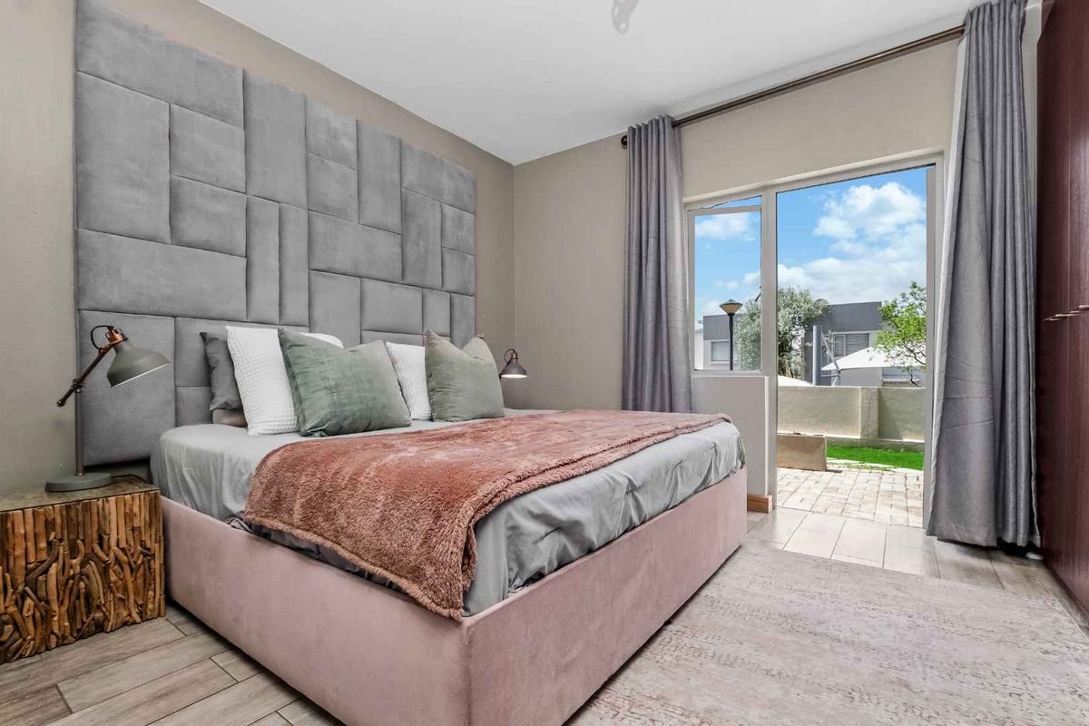 A well-maintained bedroom featuring a large upholstered headboard, tiled flooring, and direct access to an outdoor patio area through sliding glass doors.