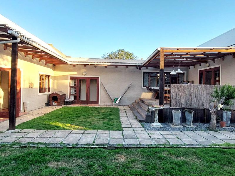 Rear view of the property featuring a paved patio area, a raised timber deck with a pergola, and access to the main living spaces.