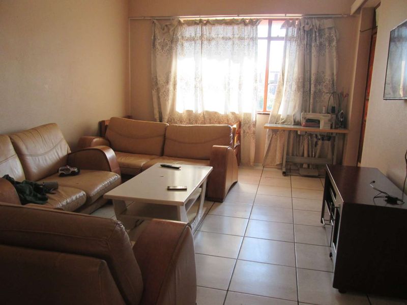 A living room featuring tiled flooring and a large window with curtain rails, providing a functional and well-lit space.
