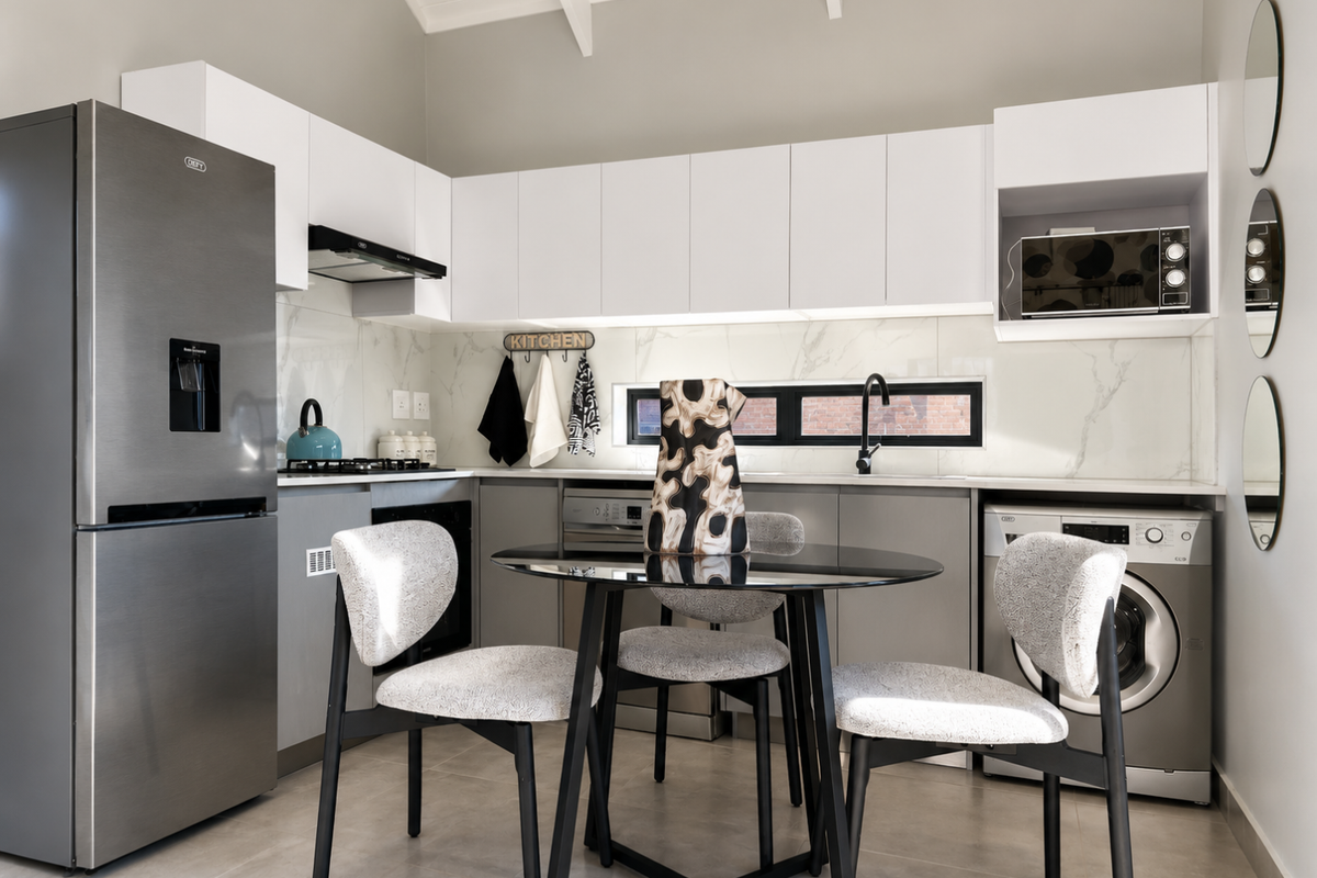 Modern kitchen featuring white cabinetry, marble-look backsplash, integrated appliances, and a vaulted ceiling, creating a bright and functional culinary space.