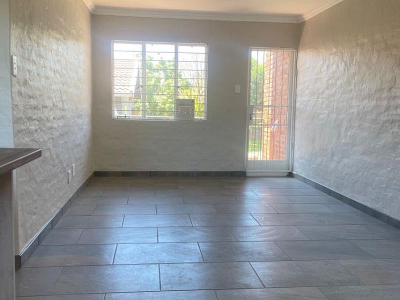 An empty living area featuring neutral tiled flooring, textured walls, and a security gate leading to the exterior.