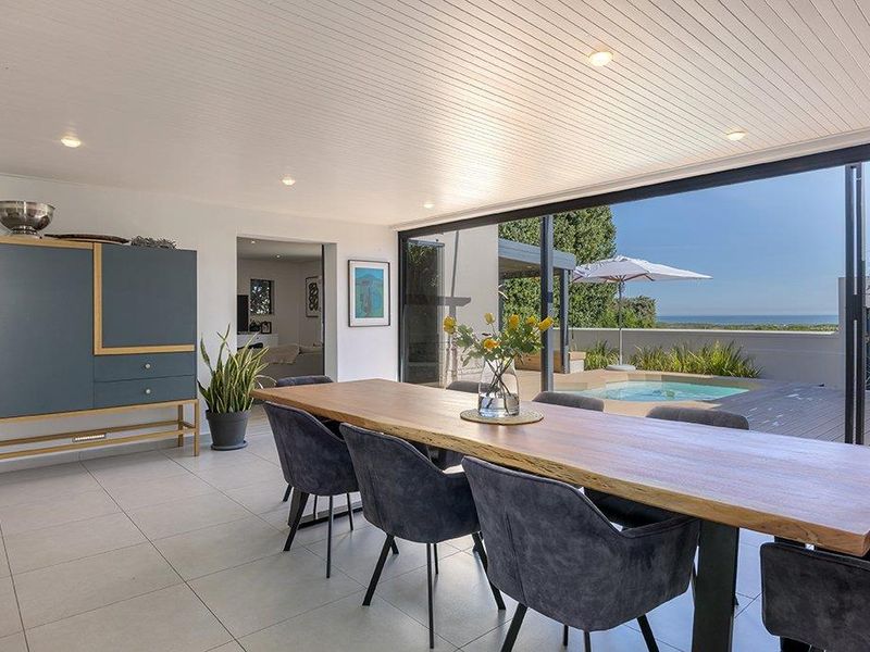 Bright open-plan dining area featuring modern tiled floors, recessed lighting, and expansive sliding doors opening onto a pool deck with ocean views.