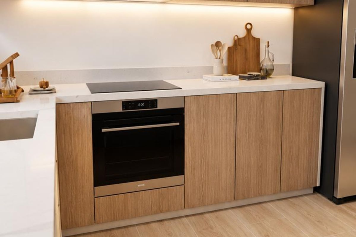 Modern kitchen featuring light wood cabinetry, stone countertops, integrated oven, induction cooktop, and stainless steel extractor fan with under-cabinet lighting.