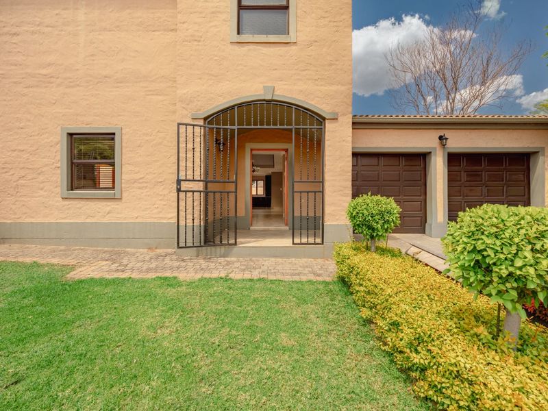 Front elevation of a two-story house featuring a double garage, security gate entrance, and a well-maintained front garden with paved walkway.