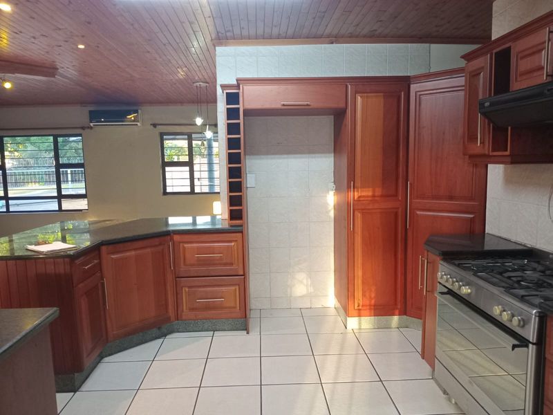 Spacious kitchen featuring wooden cabinetry, granite countertops, a gas stove with extractor fan, and a distinctive wooden ceiling, opening into the living area.