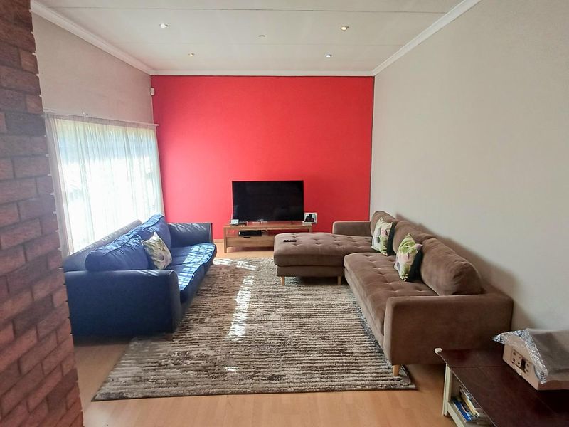 Spacious living room featuring an exposed brick wall, laminate flooring, and recessed downlighting, offering a comfortable and functional family space.