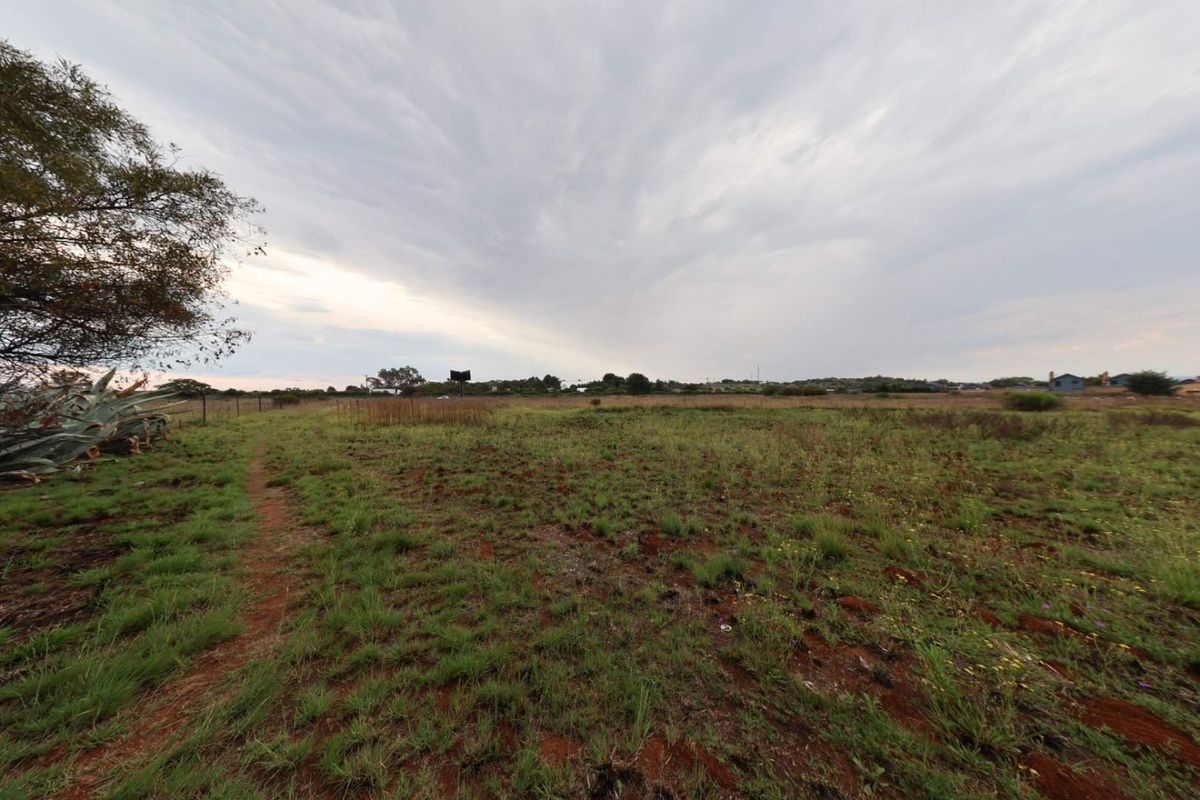 A wide-angle view of a vacant residential plot featuring natural grass cover and perimeter wire fencing under an overcast sky.
