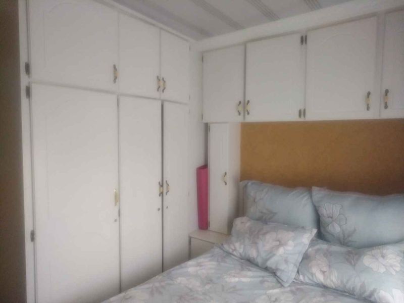 A bedroom featuring extensive white built-in cupboards and overhead storage units providing ample integrated storage space.