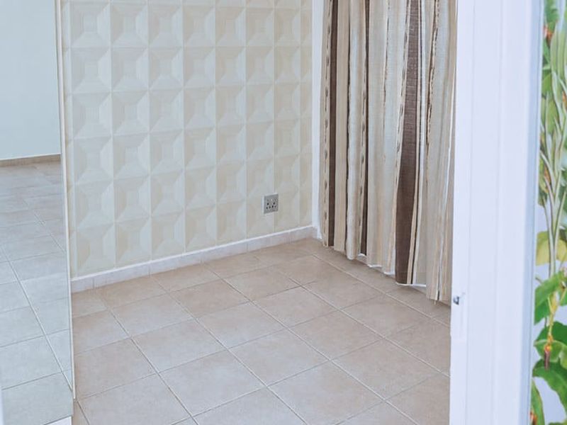 A bright, empty bedroom featuring neutral tiled flooring, a textured feature wall, and a modern pendant light fixture.