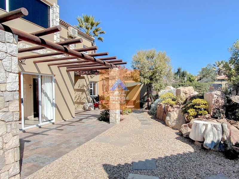Rear exterior view featuring a tiled patio with a timber pergola, stone-clad pillars, and a landscaped gravel garden with rockery elements.