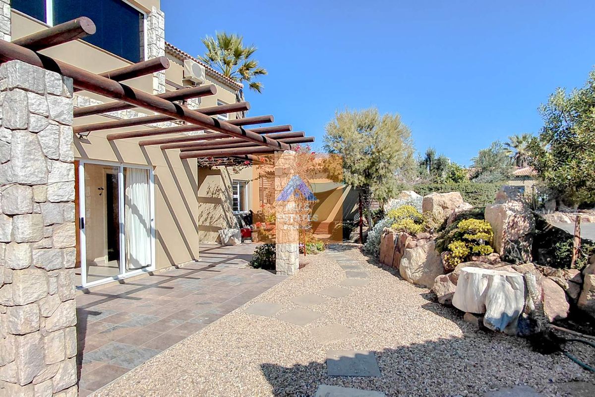 Rear exterior view featuring a tiled patio with a timber pergola, stone-clad pillars, and a landscaped gravel garden with rockery elements.