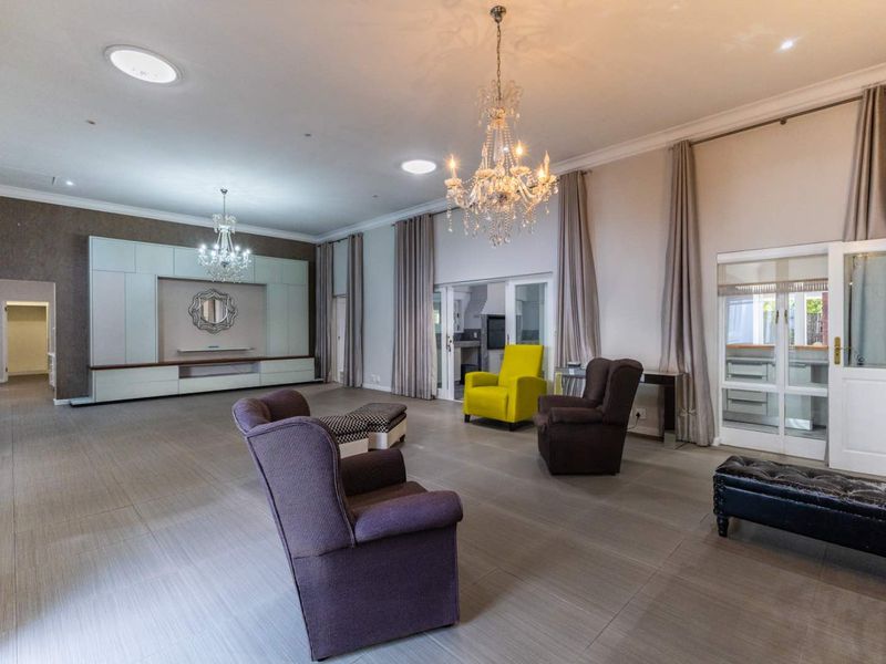Spacious living room featuring large-format floor tiles, elegant crystal chandeliers, recessed lighting, and custom built-in cabinetry with a neutral color palette.