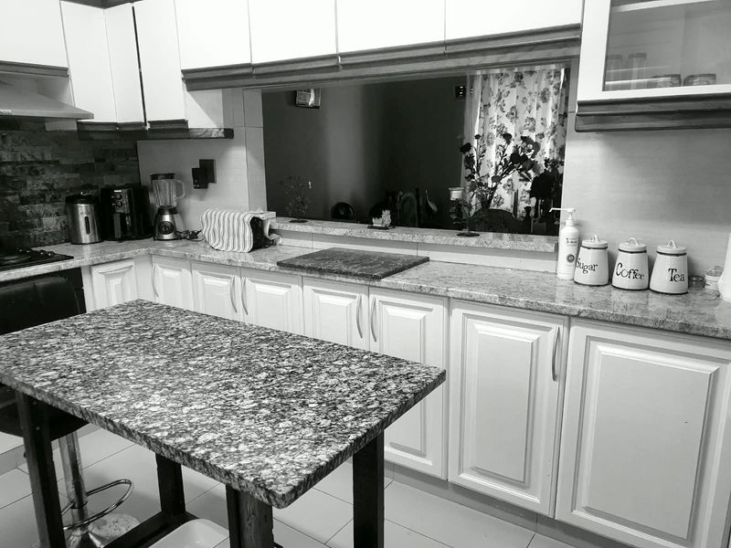 A functional kitchen featuring white cabinetry, granite countertops, and a central island, with a pass-through window connecting to the adjacent living space.