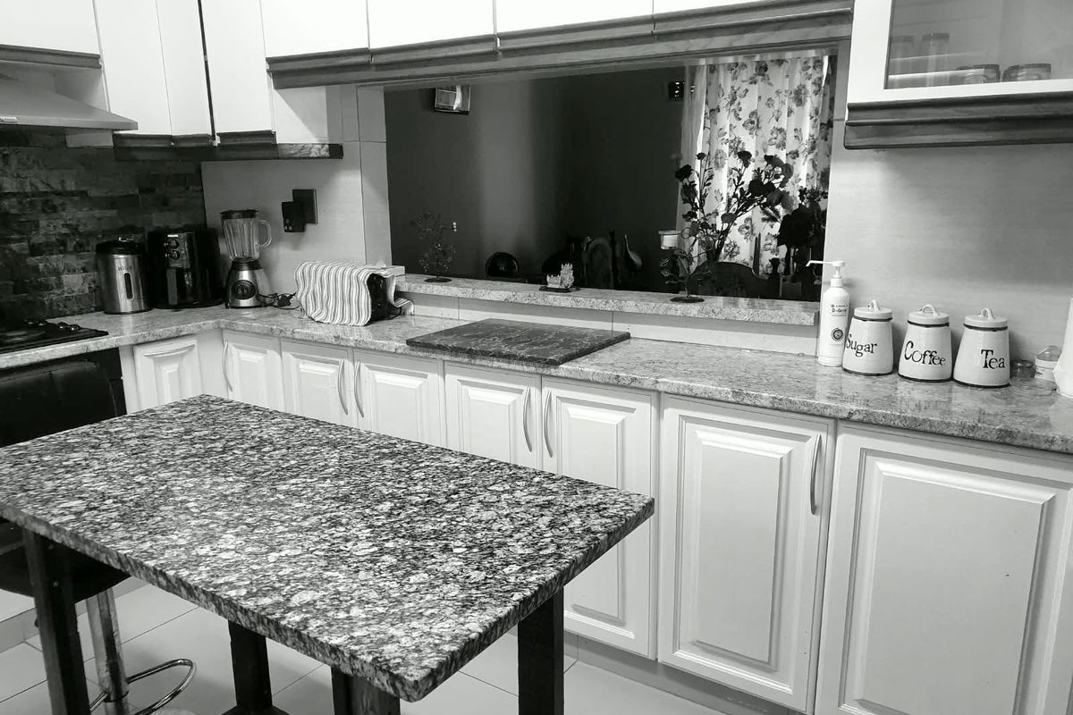 A functional kitchen featuring white cabinetry, granite countertops, and a central island, with a pass-through window connecting to the adjacent living space.
