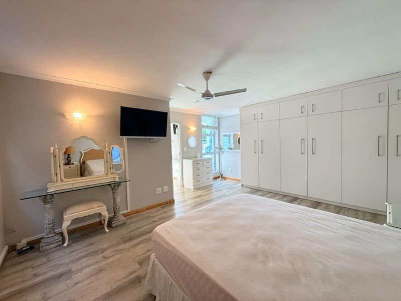 Spacious bedroom featuring extensive built-in cupboards, modern laminate flooring, and a ceiling fan, offering a clean and well-maintained living space.