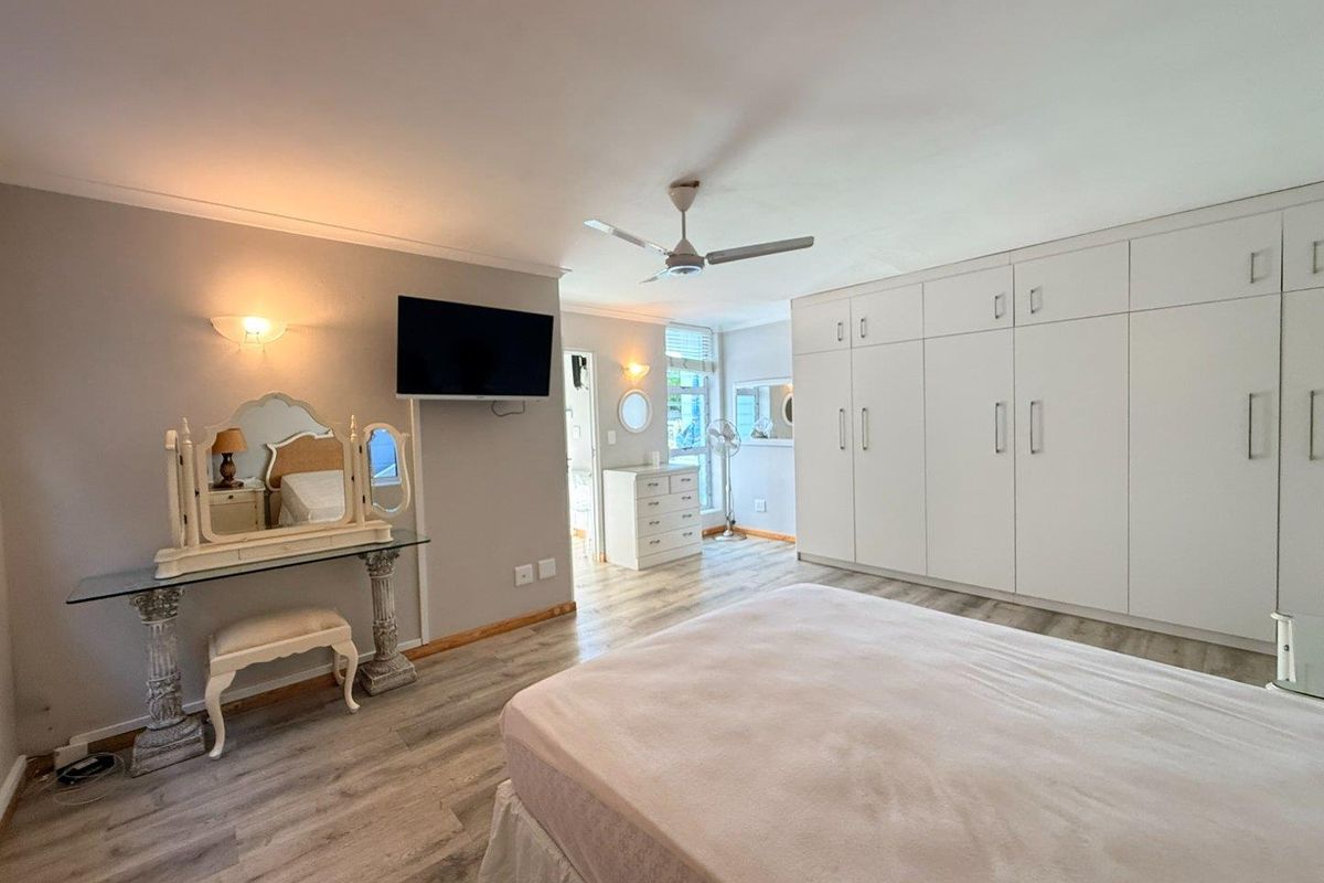 Spacious bedroom featuring extensive built-in cupboards, modern laminate flooring, and a ceiling fan, offering a clean and well-maintained living space.