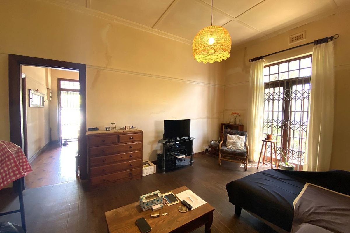 A living room featuring original timber flooring, high ceilings with decorative molding, and a large glass door with security gate leading to the exterior.