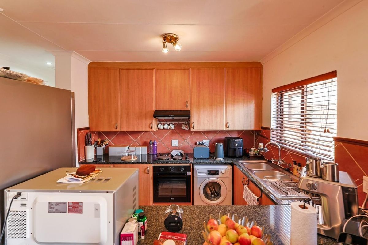 Functional kitchen featuring wood-look cabinetry, granite countertops, integrated oven, hob, extractor fan, and a built-in washing machine connection.