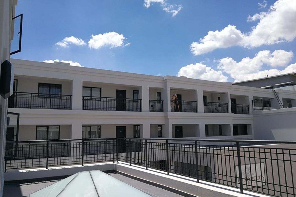 Exterior view of a modern apartment complex featuring multi-level balconies with metal railings and a prominent skylight on the terrace level.