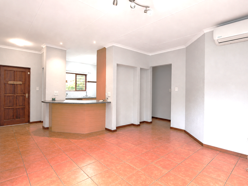 Spacious open-plan living area featuring tiled flooring, a breakfast bar, and an integrated air conditioning unit, offering a versatile layout for modern living.