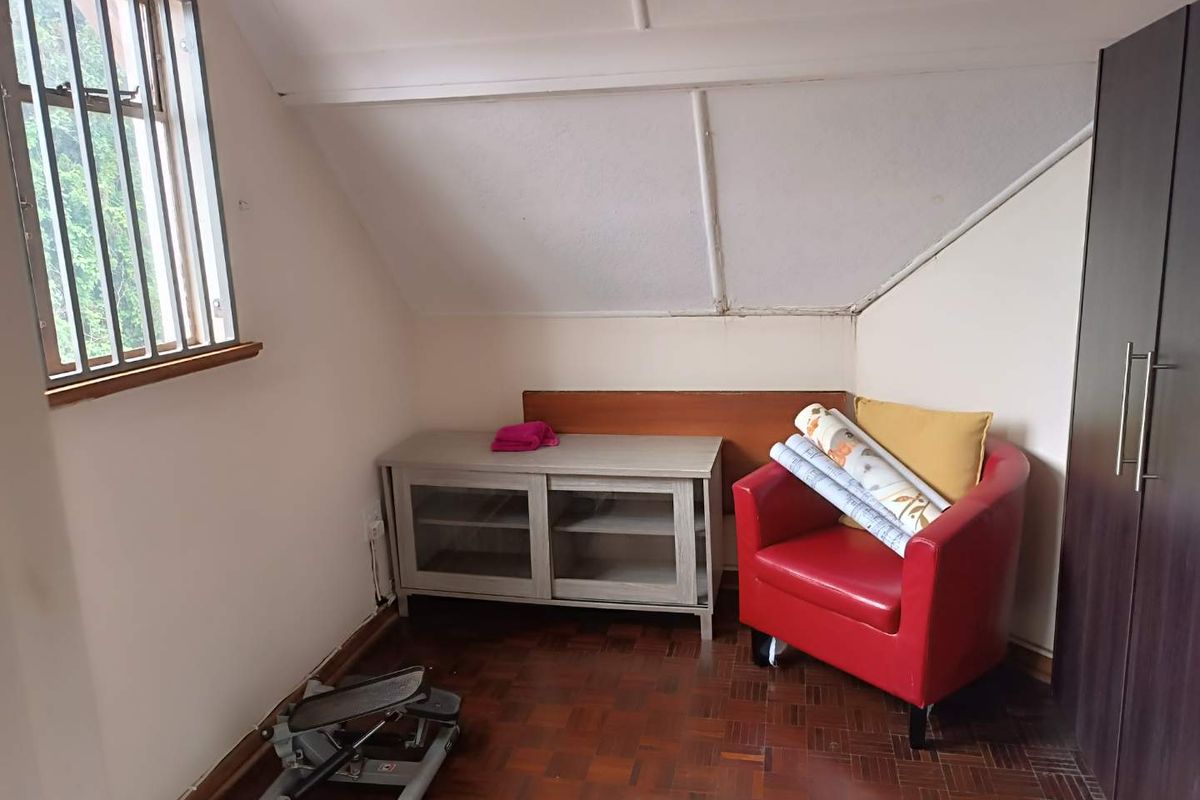 A compact bedroom featuring parquet flooring, a built-in wardrobe, and a window with security bars, set under a sloped ceiling.