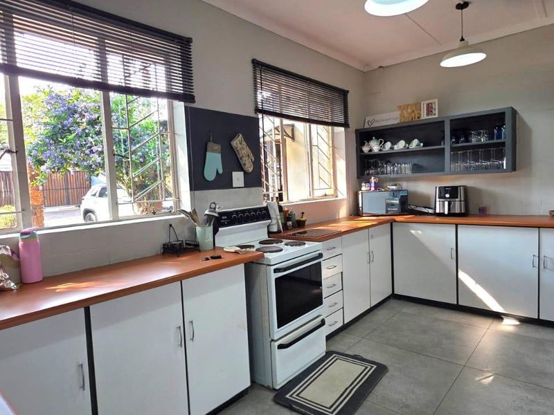 A functional kitchen featuring white cabinetry, wooden countertops, a freestanding stove, and tiled flooring, with natural light provided by large windows with security bars.
