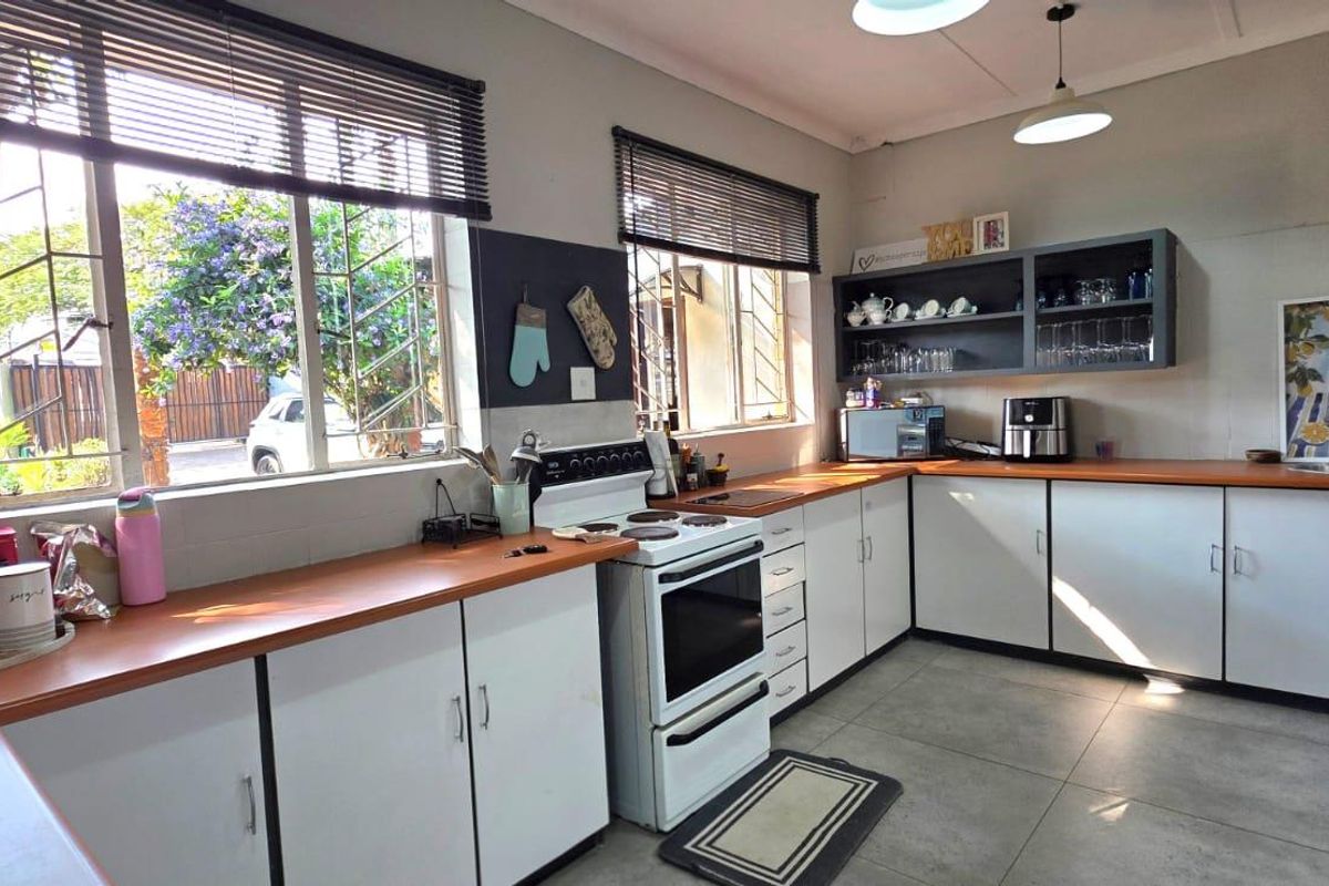 A functional kitchen featuring white cabinetry, wooden countertops, a freestanding stove, and tiled flooring, with natural light provided by large windows with security bars.