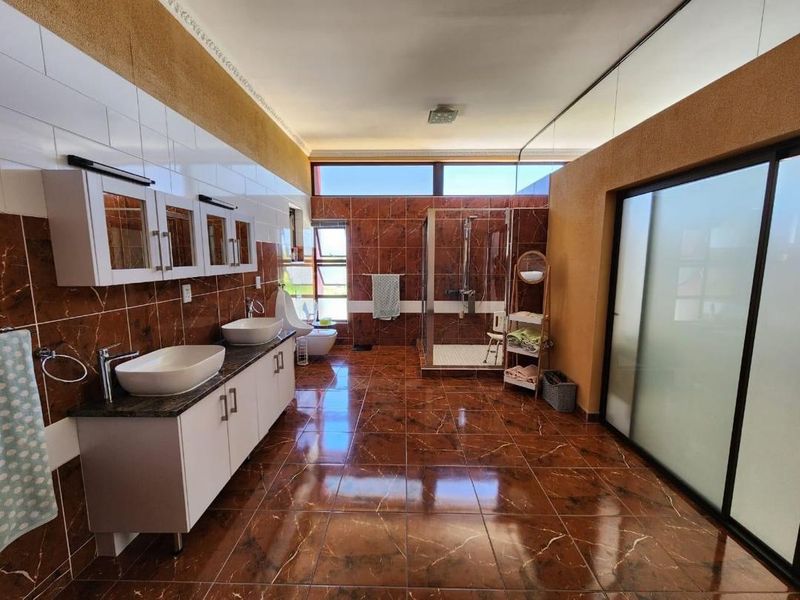 Spacious modern bathroom featuring a double vanity with vessel sinks, a walk-in shower, wall-mounted toilet, bidet, and rich brown marble-style floor and wall tiling.