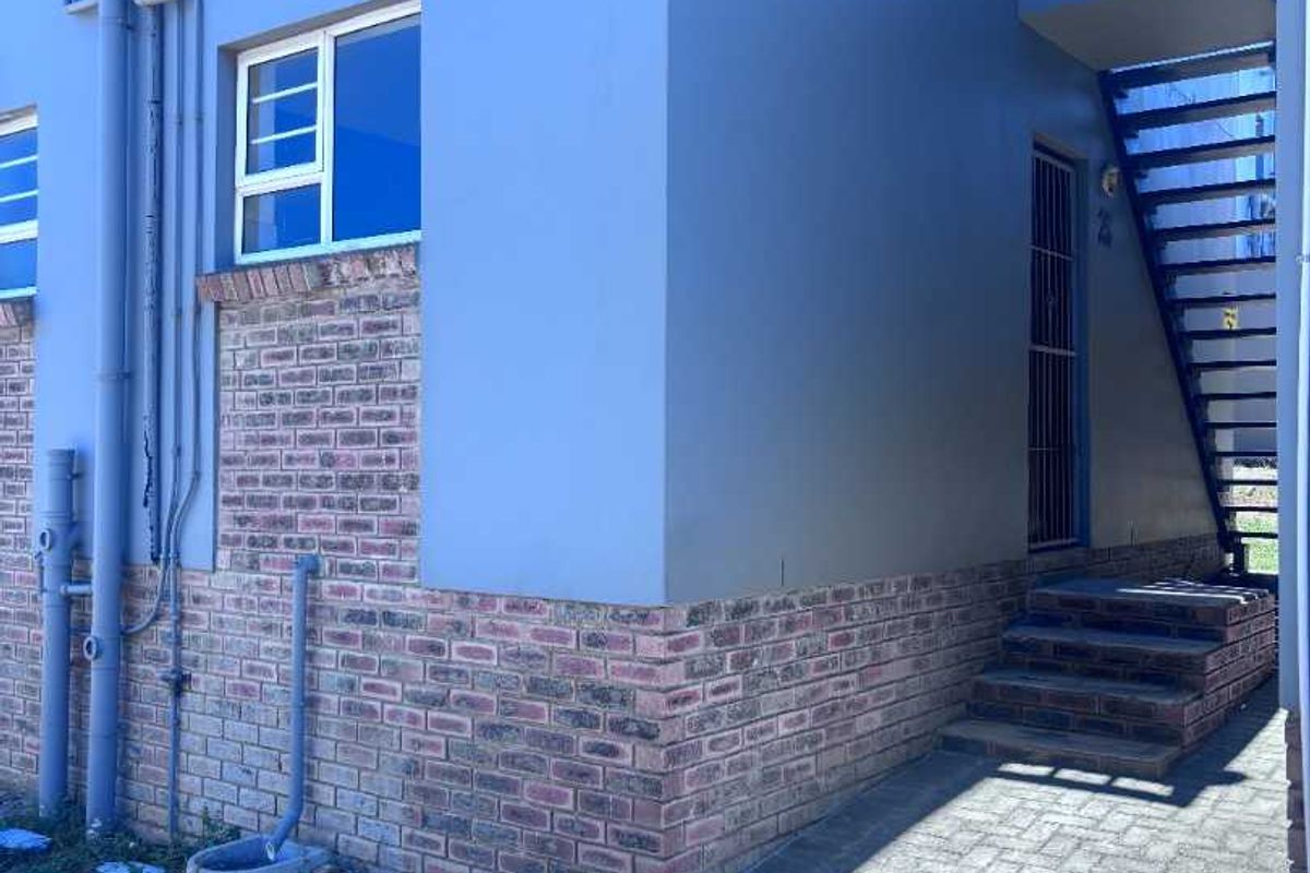 Exterior view of an apartment building featuring a brick and painted facade, external metal staircase, and paved ground area.