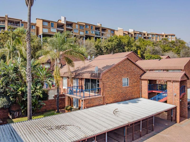 An elevated view of the apartment complex featuring brick exterior, tiled roofing, private balconies, and covered carport parking facilities.