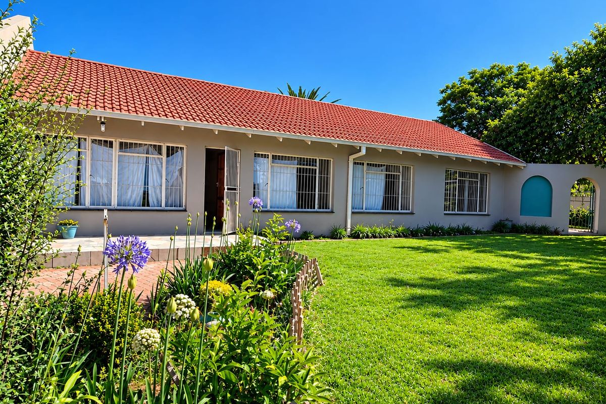 A well-maintained rear exterior view of the house featuring a terracotta tiled roof, paved patio area, and a spacious green lawn.