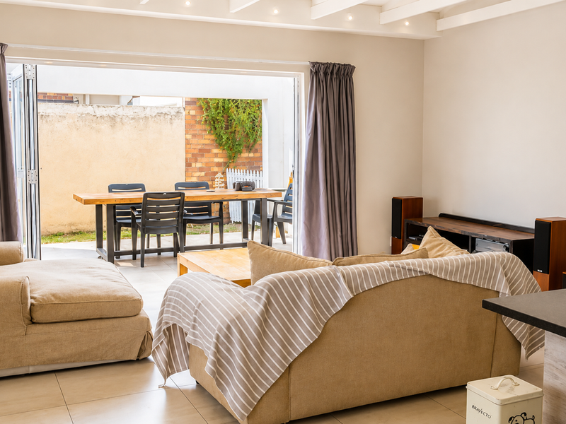 Bright living room featuring tiled flooring, exposed beam ceiling, and large bi-fold doors providing seamless access to the outdoor patio area.