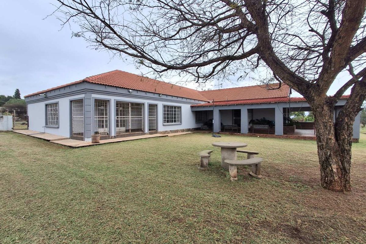 Rear view of a farm-style house featuring a covered patio, terracotta roof tiles, and security bars on windows, set within a spacious garden.