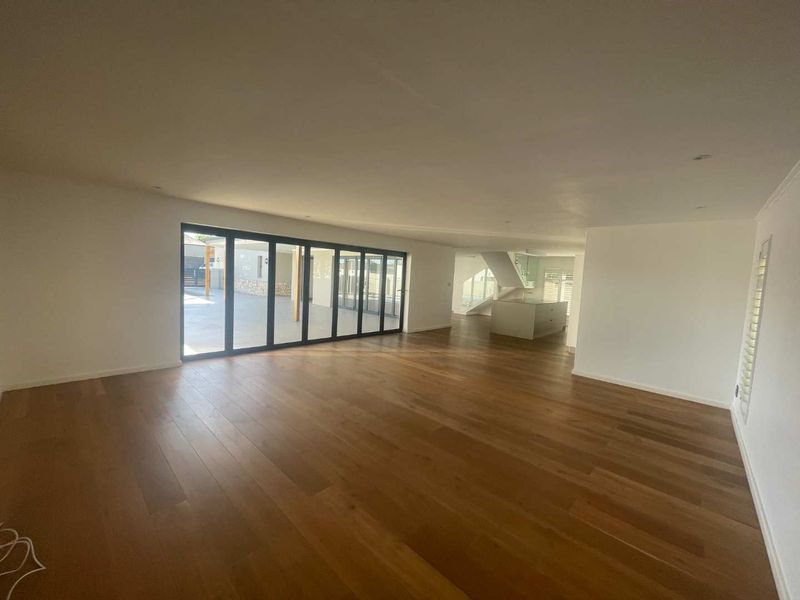 Spacious open-plan living area featuring polished timber flooring, recessed lighting, and large bi-fold doors opening to an outdoor patio.
